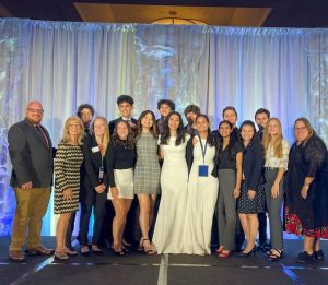 Group of adults and students stand on stage in formal attire