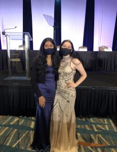 Two young women stand together in formal dresses.