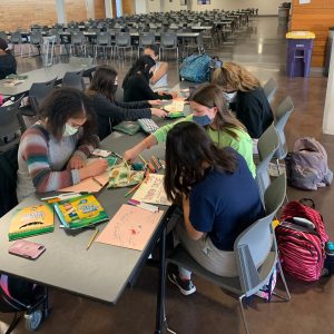 Students sit together writing on colored paper.