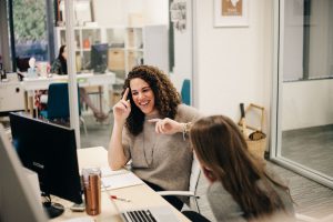 Two women sit at a computer in an office.