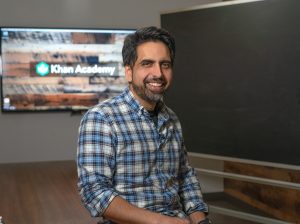 A portrait of Sal Khan in front of a blackboard and screen reading Khan Academy