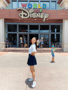 A young woman wearing a black skirt and white top poses in front of a Disney store.