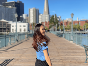 A young woman standing in front of a city skyline turns and her long hair flows around her.