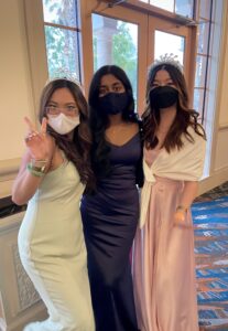 A picture of three young women posing wearing formal gowns, two wearing tiaras. 