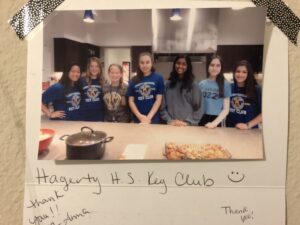 A picture of seven students wearing Key Club t-shirts standing in a kitchen with a plate and a pot in the forefront of the photo. Text on the photo reads, Hagerty H.S. Key Club. Thank you! 