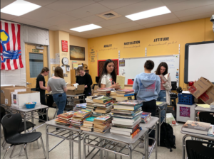 Several teenage students organize stacks of books in a classroom.