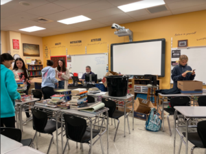 Several teenage students organize stacks of books in a classroom.