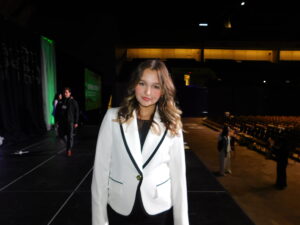Aspen stands in front of an empty auditorium looking off stage at the camera