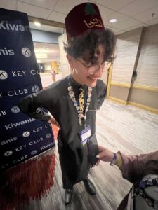 Moe stands grinning, wearing a traditional fez hat and black djubba shirt.
