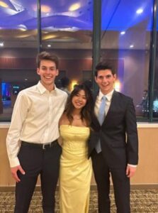 David stands smiling next to two other students wearing formal attire. 