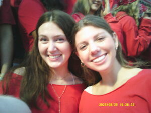 A slightly blurry photo of two young people smiling while wearing red surrounded by other people wearing red.