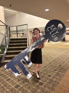 A young person stands holding a cutout of a key that is larger than she is.