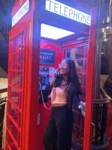 A young person stands in a bright red old fashioned phone booth holding the receiver 