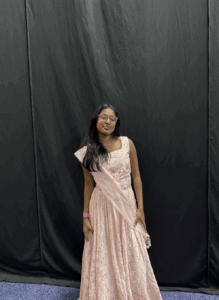 A young person is standing wearing a light pink lace dress and stole 