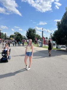 1.	A young person stands at an outdoor festival with a crowd behind her.