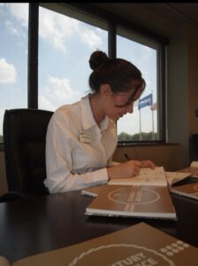 A young person wearing a white button up shirt signs a book 