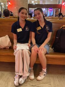Two young people sit side by side wearing the same navy shirt and gold name tags. 