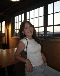 A young person sits back smiling in front of big windows 