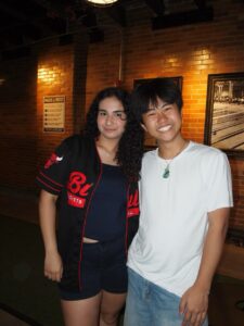 Two young people stand arm in arm smiling