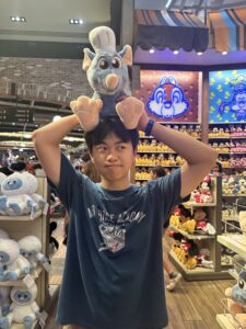 A young person stands in a colorful store holding a stuffed animal on his head.