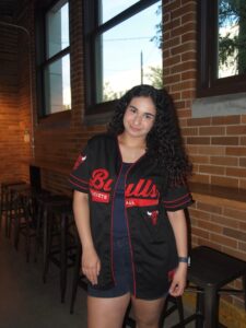 A young person stands wearing a Bulls shirt standing in front of a brick wall.