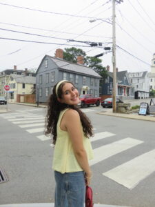 A young person smiling over her shoulder standing in a crosswalk wearing a yellow shirt and headband.